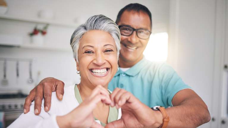 older couple making heart with hands in kitchen | cosmetic dentist lakeville mn