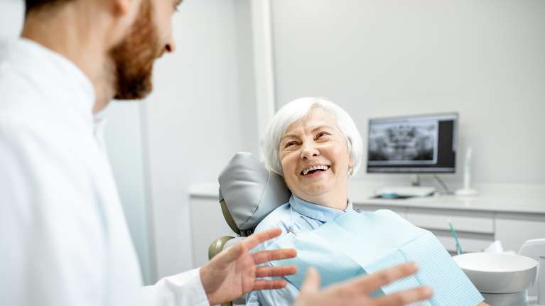 older woman sitting in dentist exam chair | dental implants lakeville mn